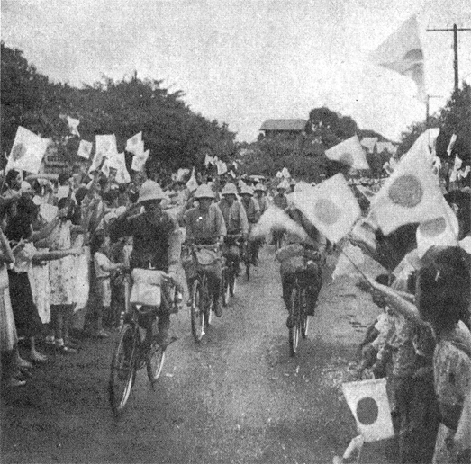 Japanese troops bicycling through a crowd of Filipinos waving Japanese flags