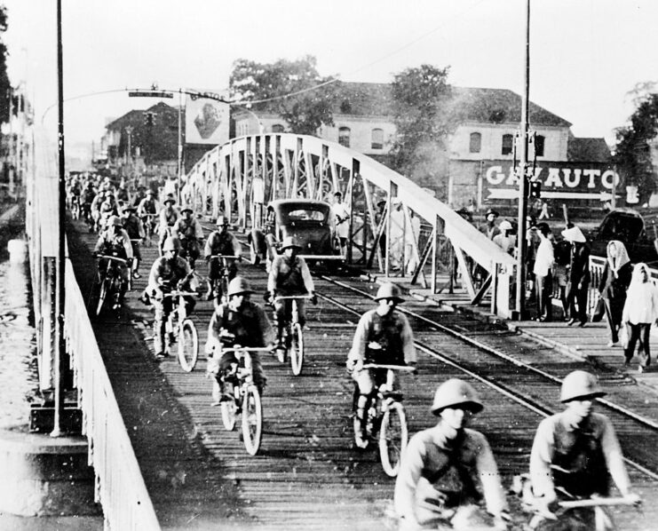 Japanese troops bicycling over a wooden bridge