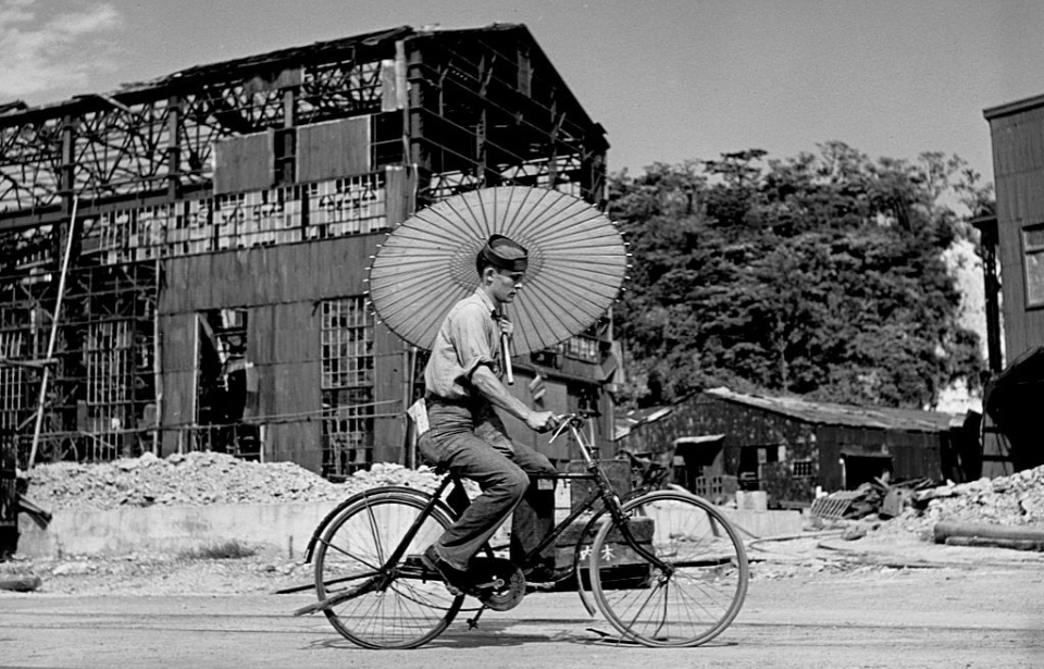 Man riding a bicycle while holding an umbrella