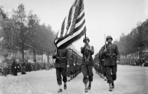 Soldiers marching down the streets of Paris while waving an American flag