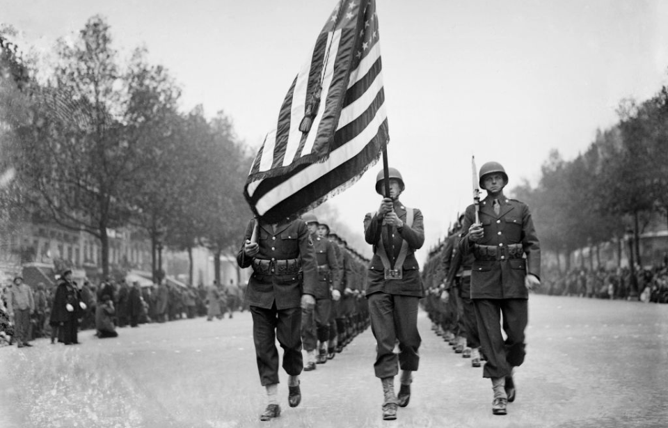 Soldiers marching down the streets of Paris while waving an American flag