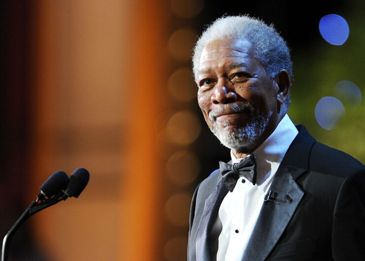 Morgan Freeman standing at a pair of microphones