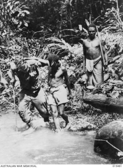 Jerry Cronin and two "Fuzzy Wuzzies" walking across a river in the middle of the jungle