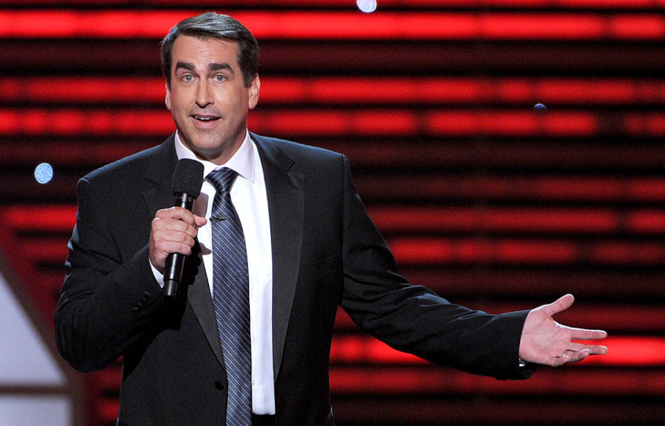 Rob Riggle speaking into a microphone on stage