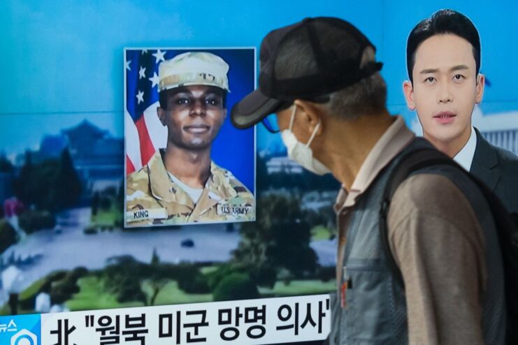 Man walking by a television screen showing a news report about Travis King