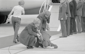 Two nurses standing around Gail Kerns as he kisses the tarmac at Andrews Air Force Base, Maryland