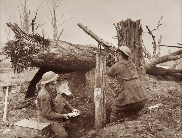 Australian soldier aiming a Lewis gun from behind a tree while another holds ammunition