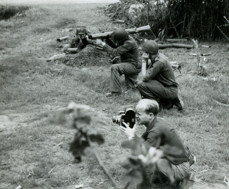 Swedish soldier operating an M1 Carl Gustaf infantry anti-tank weapon while two others cover their ears and one mans a camera