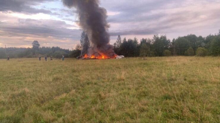 Crashed Embraer aircraft shrouded in flames and smoke in a grassy field