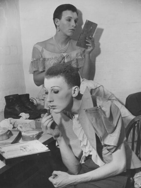 Two men applying makeup while dressed in drag