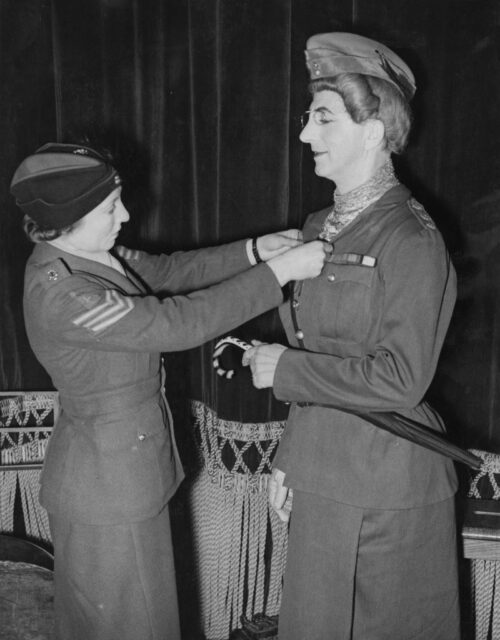 Woman buttoning up the jacket of a Douglas Byng, who's dressed as a female service member