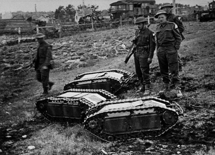 Four British soldiers standing around three Goliath tracked mines