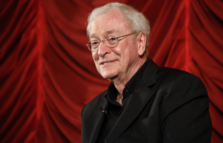 Michael Caine smiling in front of a red backdrop