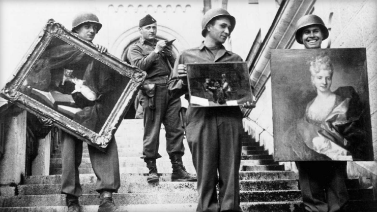 Three Monuments Men holding paintings while a military officer stands behind them