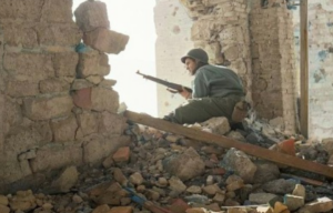 American sniper looking through a gap in a broken wall