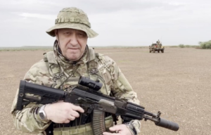 Man believed to be Yevgeny Prigozhin standing in the middle of a desert area in military fatigues, holding a weapon