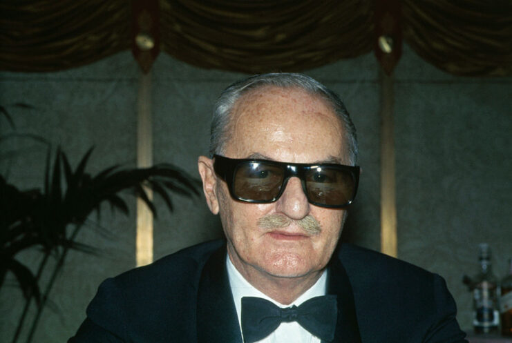Darryl Zanuck wearing a suit and sunglasses