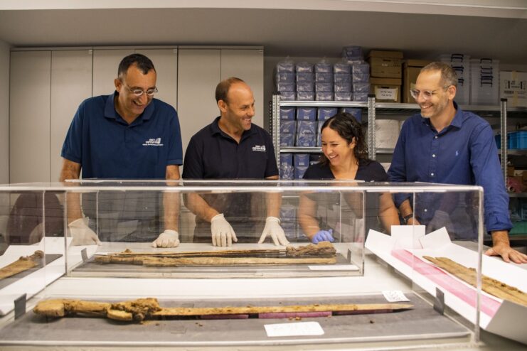 Dr. Asaf Gayer, Oriya Amichay, Dr. Eitan Klein and Amir Ganor standing around glass containers holding Roman-era swords