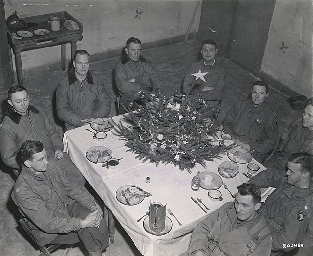 Nine American soldiers sitting around a table with a small Christmas tree at the center