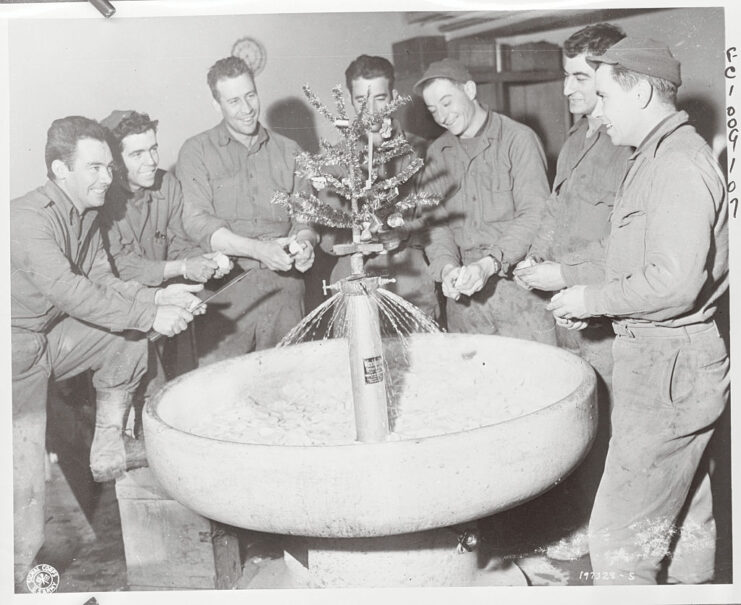 Seven soldiers with the 101st Airborne Division peeling potatoes around a sink with a Christmas tree in the center