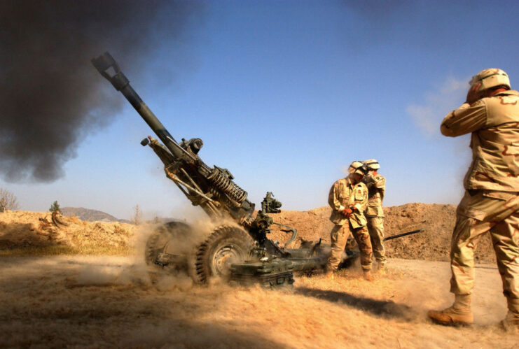 US Army soldiers covering their ears as a 105 mm Howitzer is fired