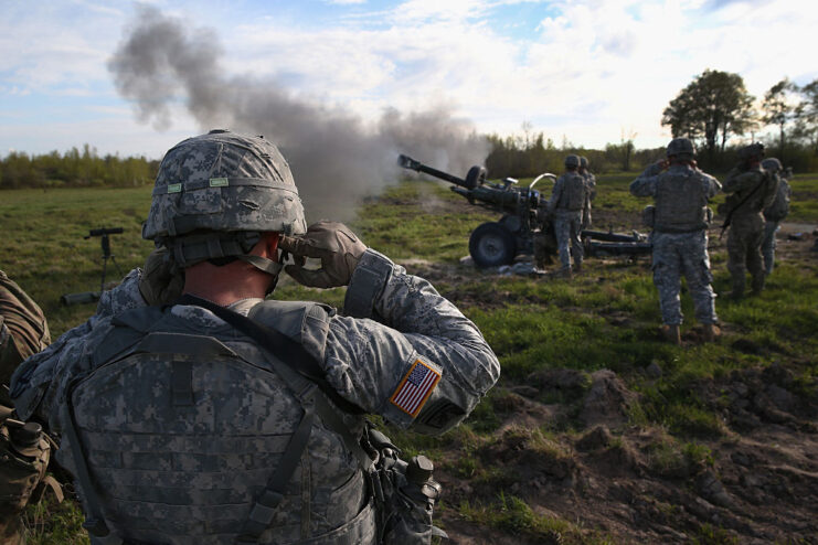 10th Mountain Division soldiers standing around a 105 mm Howitzer while it's being fired