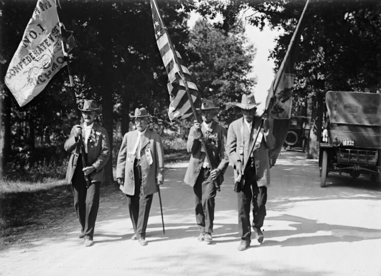 Four veterans walking down a road carrying flags on poles