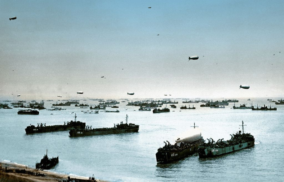 Ships anchored off the coast of Omaha Beach, while barrage balloons float overhead