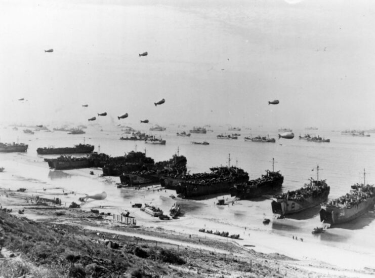 Ships anchored off the coast of Omaha Beach, while barrage balloons float overhead