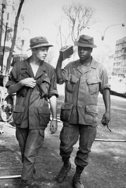 Two US servicemen walking down a street while listening to a portable radio