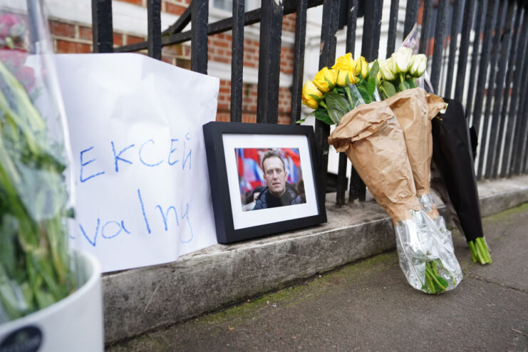 Flowers, paper and a photo of Alexei Navalny leaned up against a metal gate