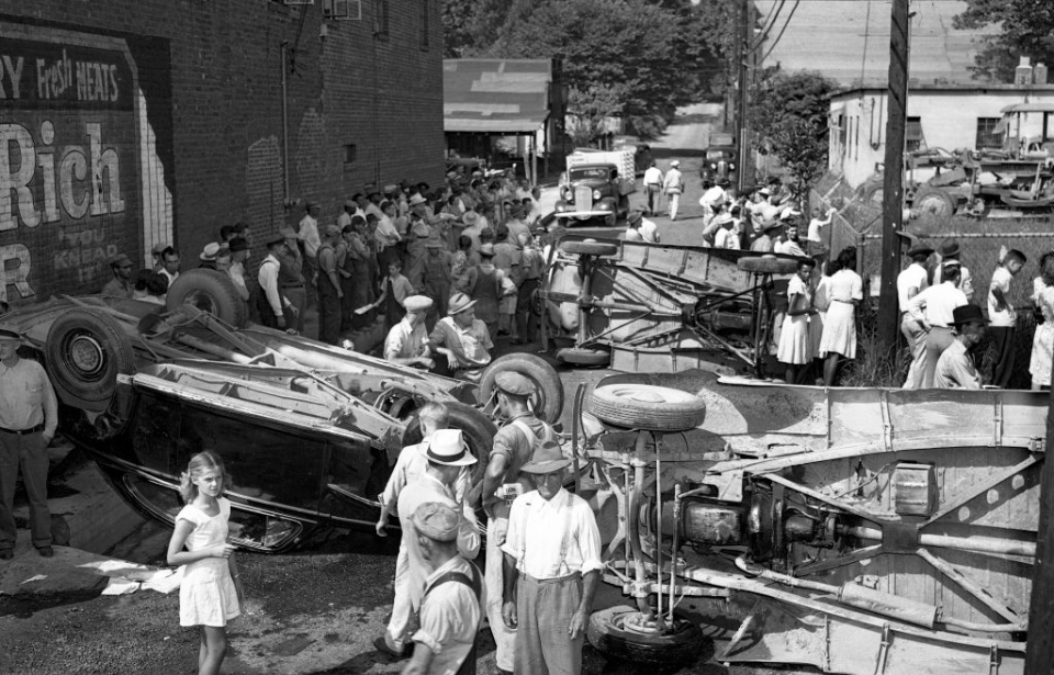 Crowd standing among overturned vehicles in the middle of a street