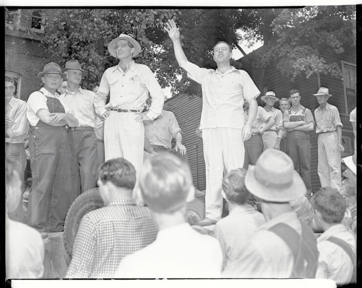 Crowd standing around Rev. Bernie Hampton, who is standing on an overturned vehicle