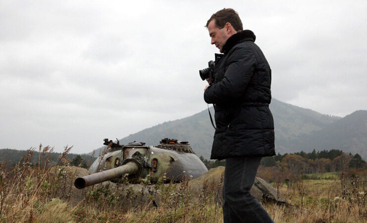 Dmitry Medvedev walking by a disabled tank turret in the grass