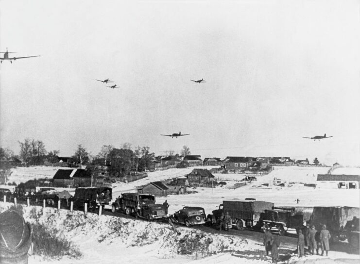 German soldiers and military vehicles moving along a road while aircraft fly overhead