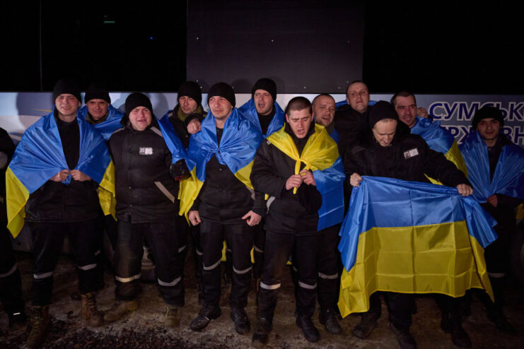 Ukrainian soldiers standing together with Ukrainian flags draped over their shoulders