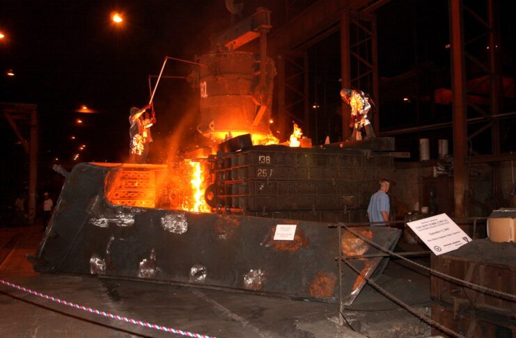 Workers standing around a machine melting steel