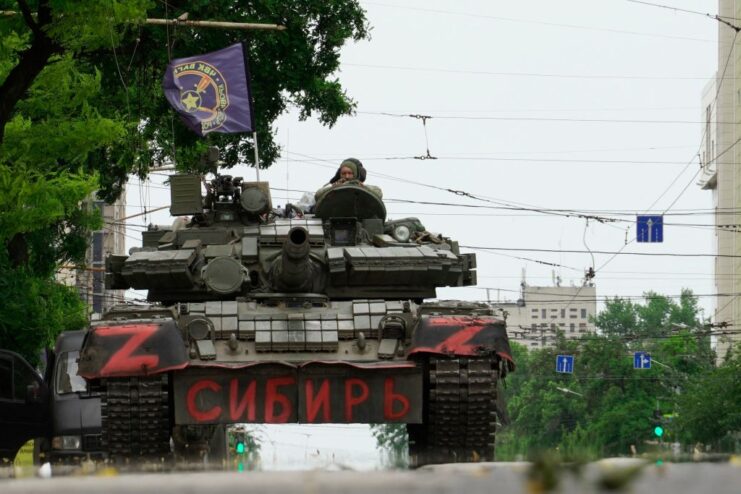 Wagner PMC mercenaries sitting atop a military tank in the middle of a city street