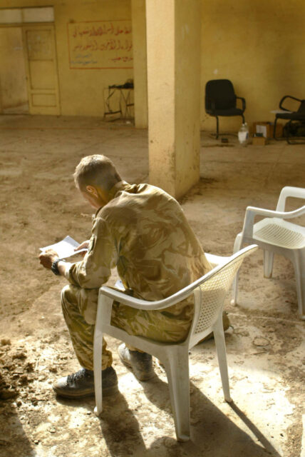 Lance Cpl. Grant Yates reading a letter while sitting in a white plastic chair