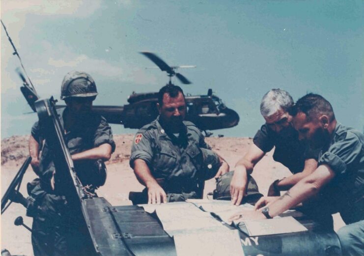 Chaplain Lewis, Lt. Col. Dionne, Brig. Gen. Young and Lt. Col. Barker reading documents laid out on the hood of a Jeep