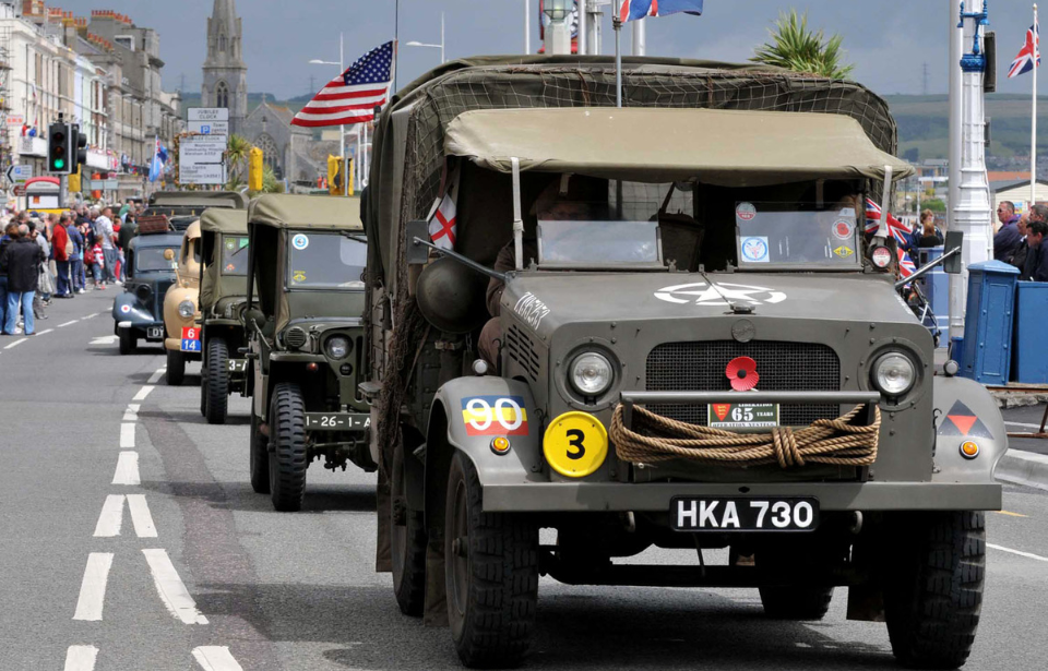 World War II-era vehicles driving down a street in the middle of a town