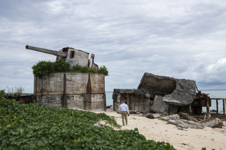 Man standing beneath a large World War II-era gun on the coast of Betio island