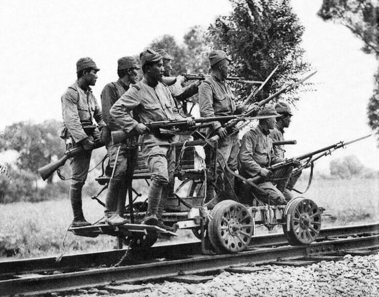 Japanese soldiers equipped with Type 38 rifles riding on a railway cart down a track