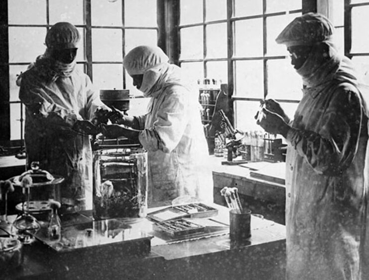 Three Japanese scientists standing around a table with equipment placed atop it