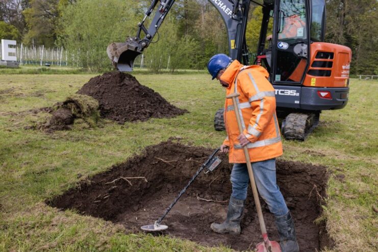 Man standing in a recently-dug hole with a metal detector
