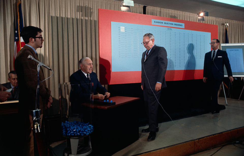 Men standing on stage with a jar filled with blue capsules and a large board