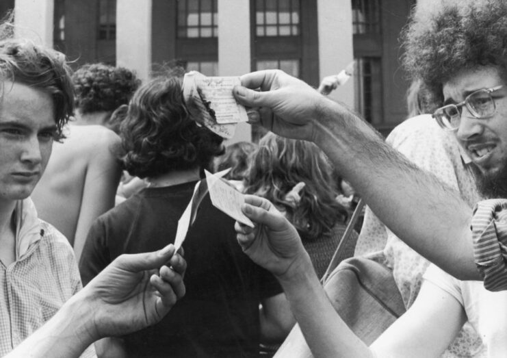 Three men burning their draft cards in the middle of a crowd