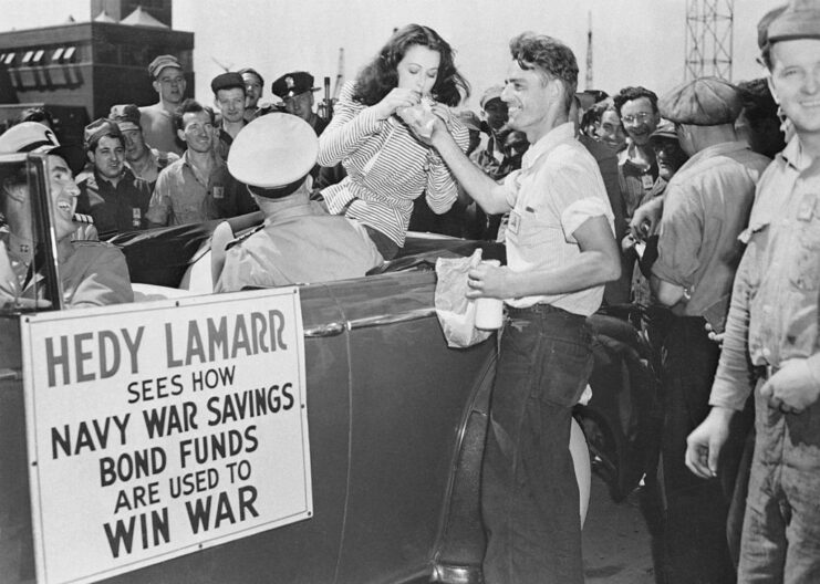 Shipyard workers watching Richard Spencer feed Hedy Lamarr a sandwich