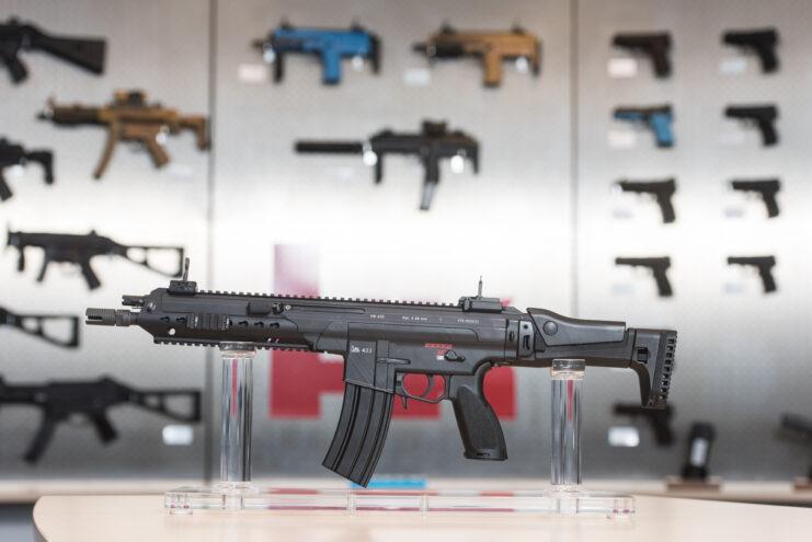 HK 433 in front of a wall of other weapons.