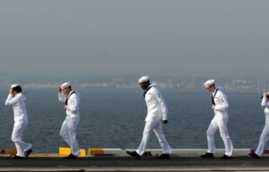 Image of 5 sailors walking along the water.